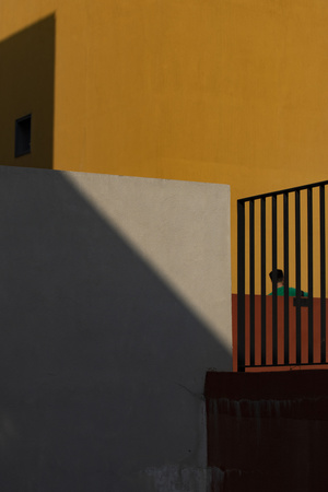 一个人站在一栋黄色建筑前的小阳台上 墙上有阴影