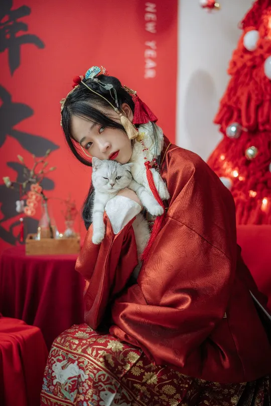 一位穿着红色和服的女人抱着一只白色的小猫站在圣诞树前面