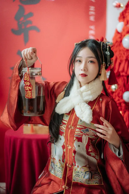 一位穿着传统服装的年轻女子在圣诞树前拿着一瓶饮料。