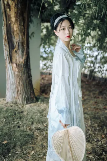 一个穿着传统白色和服的女孩拿着雨伞站在森林中