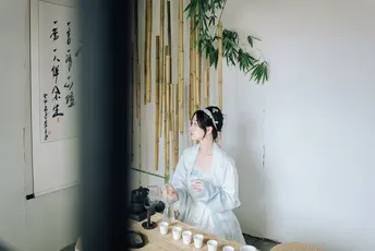 一个女性坐在桌子前 面前放着一杯茶 站在镜子前。