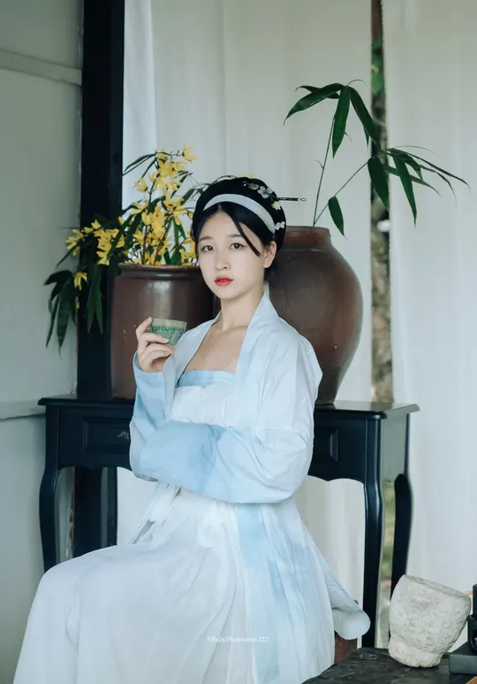 一位穿着传统白色连衣裙的年轻女子 手里拿着一束花 坐在椅子上。