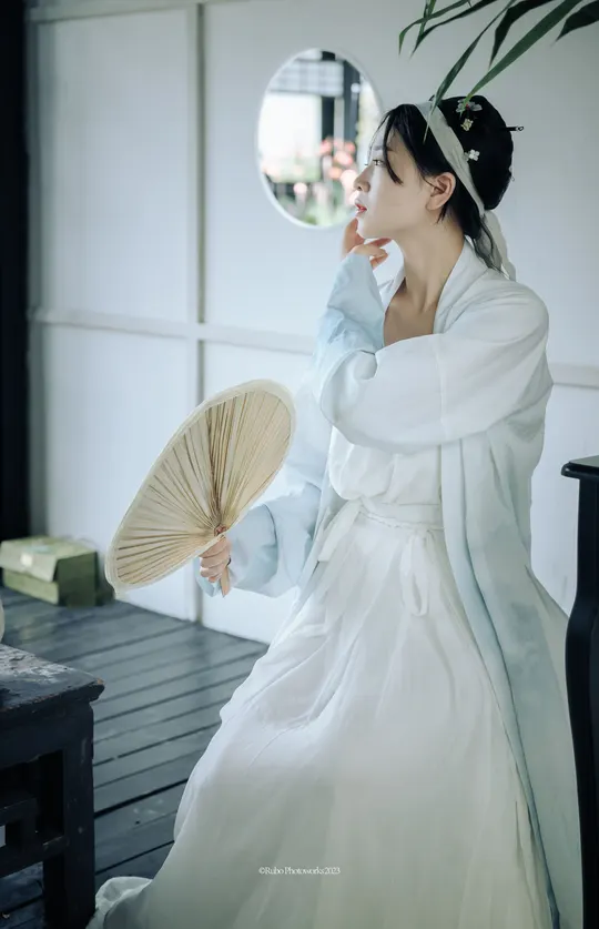一位穿着传统服装 手持扇子的女性站在镜子前