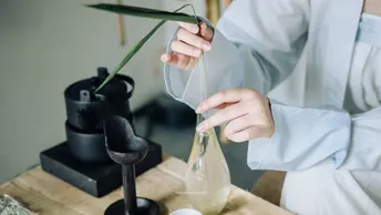 一个人穿着实验室外套 正在桌子旁边给花上的一个袋子里装液体。