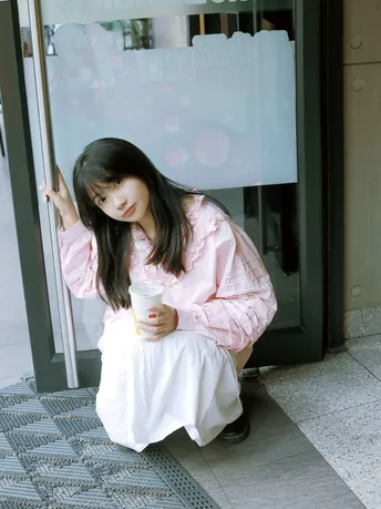 一位穿着粉红色衬衫的年轻女子坐在外面。