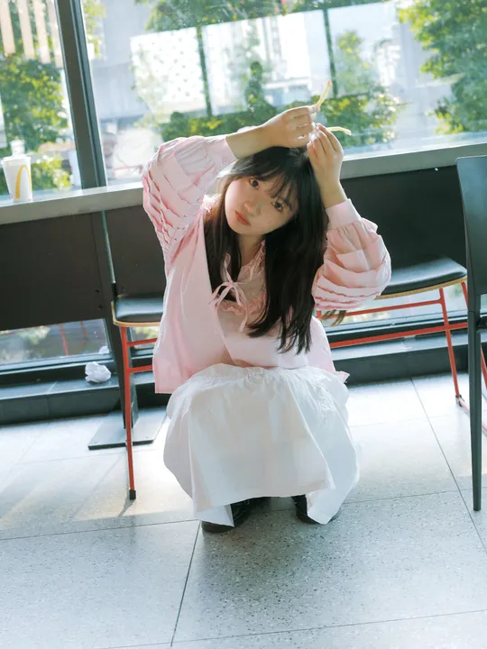 一个穿着白色连衣裙的年轻女子坐在靠近窗户的椅子上 带着一把伞。