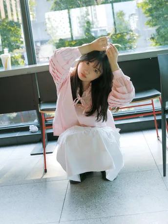 一个穿着白色连衣裙的年轻女子坐在靠近窗户的椅子上 带着一把伞。