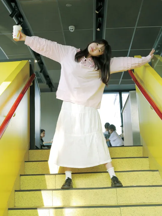 一位穿着连衣裙的年轻女子手持一个杯子站在黄色楼梯上