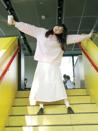 一位穿着连衣裙的年轻女子手持一个杯子站在黄色楼梯上