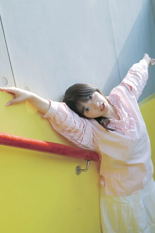 一个穿粉红色衣服的女孩正在攀爬一个黄色墙壁的游乐场。