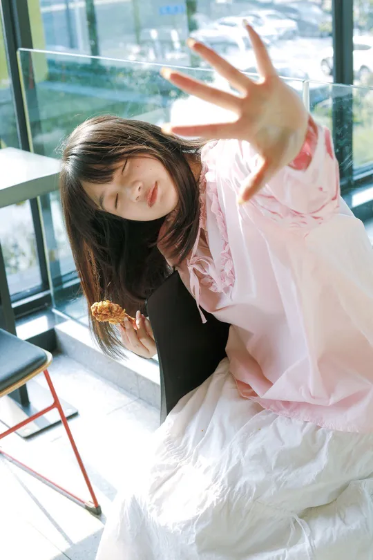 一位穿着粉红色连衣裙的年轻女子在窗户前摆姿势