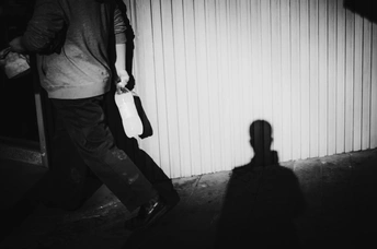 一个提着手提箱的男人晚上走在黑暗的街道上 他的影子在他身后的墙上