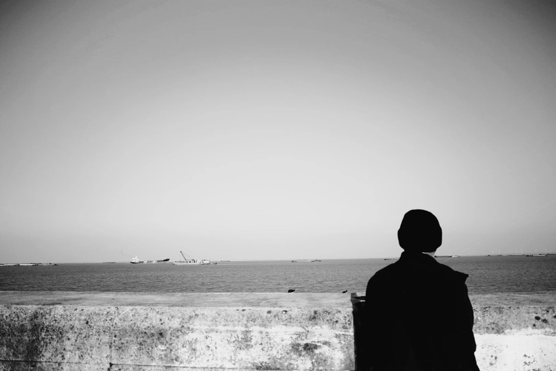 一个提着手提箱的男人站在墙上眺望大海 远处放着风筝的黑白照片