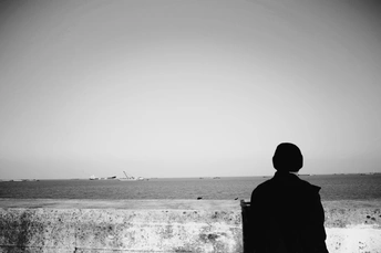 一个提着手提箱的男人站在墙上眺望大海 远处放着风筝的黑白照片