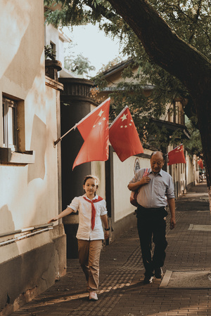 一个男人抱着一个小孩走在狭窄的街道上 一个小男孩举着红旗