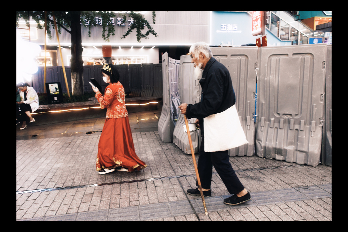 一个老人拿着棍子 和一位穿着老式裙子的老年妇女一起走下街道。