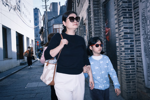 一位女士戴着太阳镜 抱着小女孩走在小巷的人行道上。