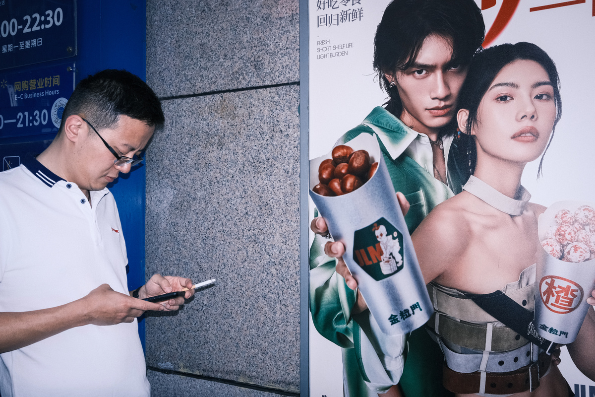 一个男人正在看墙上的广告 手里拿着手机。