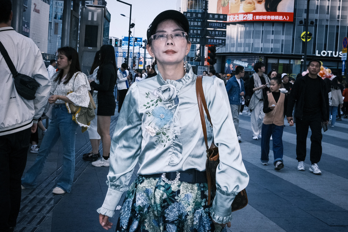 一个戴眼镜的年轻女子站在人群中的行人队伍中 沿着繁忙的城市街道走。