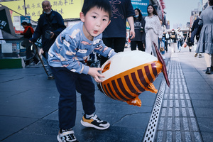一个男孩在繁忙街道人行道上玩球。
