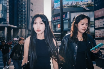 一个长发年轻女子站在繁忙的城市街道人行道上 同时看着手机