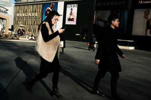 一个人和一个女人在城市人行道上走 同时看手机。