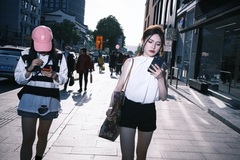 一个年轻女子站在人行道上 看着她的手机 而其他人沿着街道走。