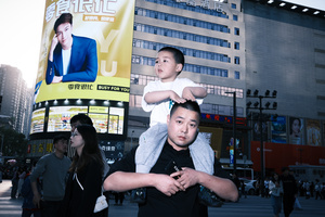 一位女子抱着一个小男孩站在城市的一栋大楼前 其他人站在街道上 女子在广告牌前摆姿势。