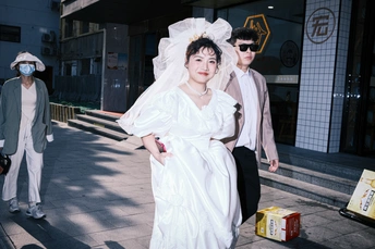 一位穿着白色连衣裙的女人戴着面具 和一位穿着婚纱的男人一起走在街上。