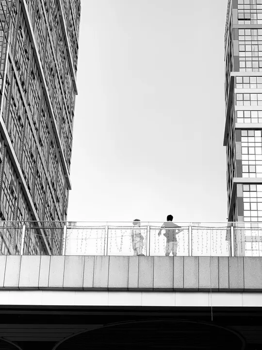 一个人站在一座城市的桥上 拿着伞 周围有高大的建筑。