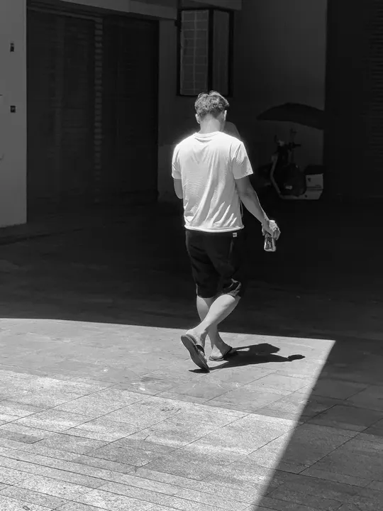 一个年轻人走在街上 带着滑板和雨伞。