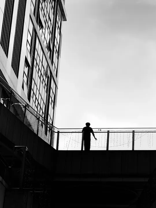 一个黑白剪影 一个人骑着滑板在桥上 背景是高大的建筑物。