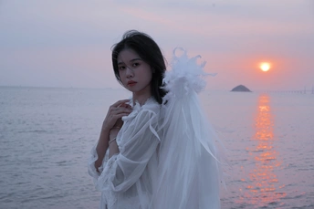 当太阳落在海面上时 一个穿着白色连衣裙和面纱的女人站在海滩上