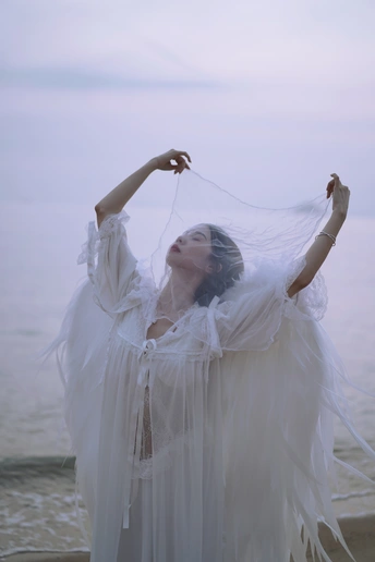 在海边的海滩上 一个穿着带面纱的白色连衣裙的女人