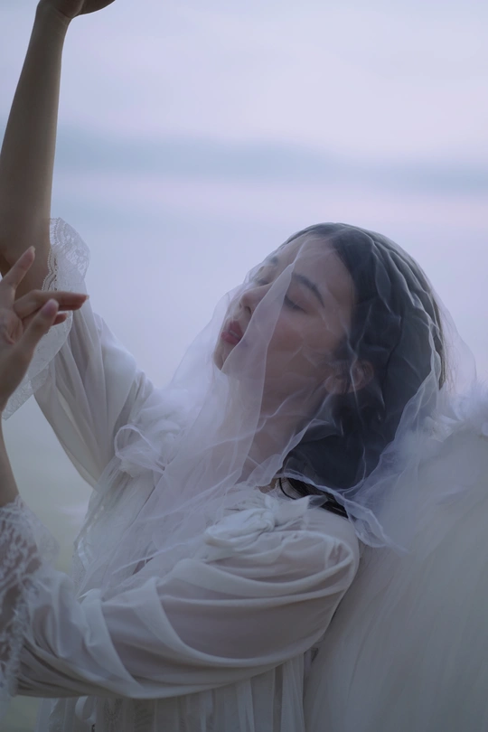 一个穿着白色连衣裙和面纱的女人把手伸向天空