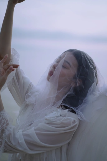 一个穿着白色连衣裙和面纱的女人把手伸向天空