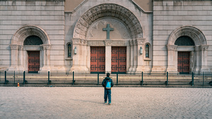 一个人站在一个有十字架的大楼的庭院里 前面有人在走。