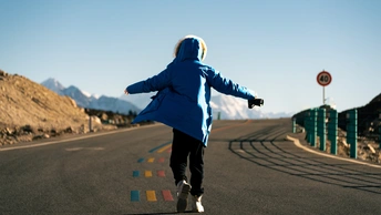 一个穿着蓝色夹克的人在山丘背景下的道路上奔跑