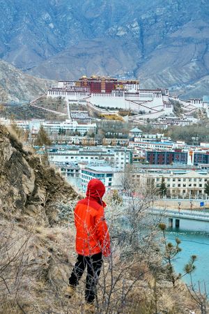 一个穿橙色夹克的男人站在一个俯瞰城市和山脉的山头上