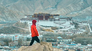 一个穿红夹克的男人站在山顶的一块岩石上 俯瞰着城市。
