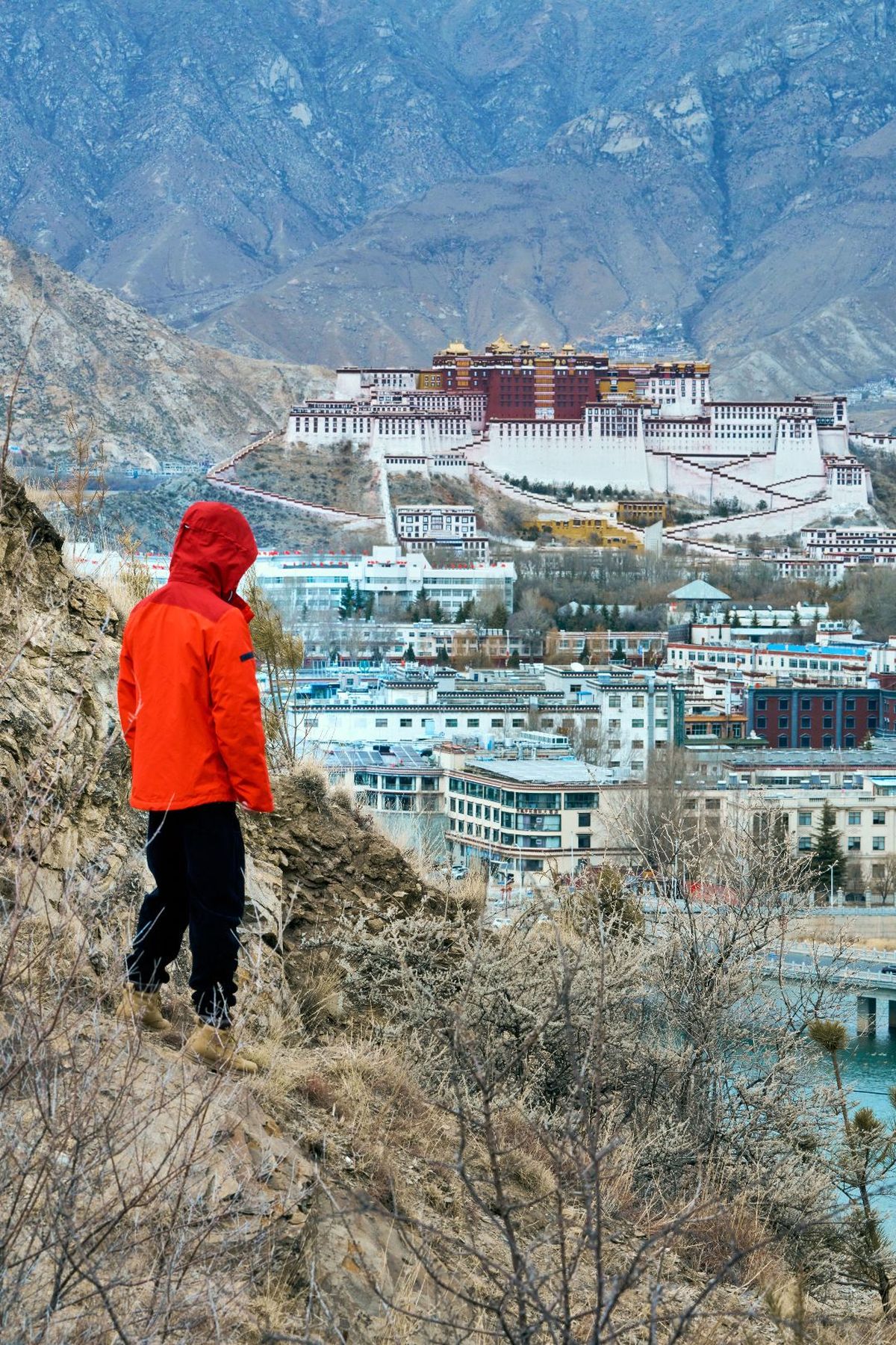 一个穿红夹克的男人站在俯瞰城市的山丘上