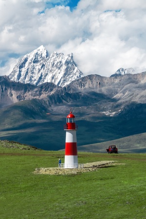 红白相间的灯塔 位于绿草地上 背景是山脉。