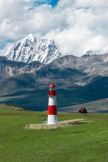 红白相间的灯塔 位于绿草地上 背景是山脉。