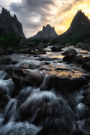 河中的岩石上流动的水在日落时 背景是山脉。