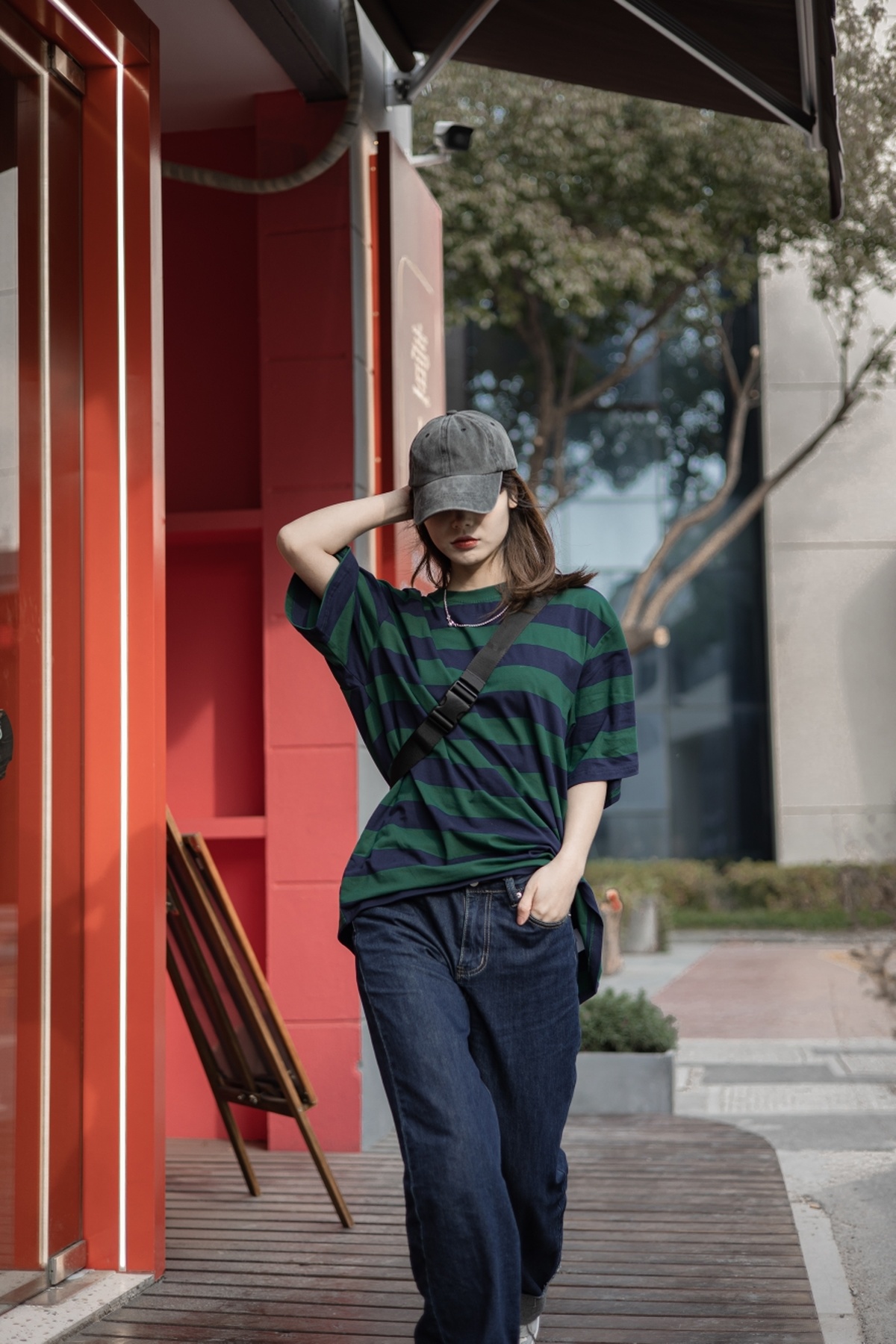 一个穿着条纹衬衫、戴着条纹帽子的年轻女子走在一栋红色建筑旁的人行道上