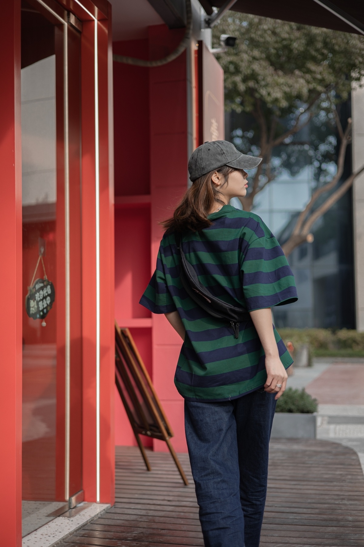 一个穿着条纹衬衫和绿色牛仔裤的年轻女子从一栋红色的大楼里走了出来
