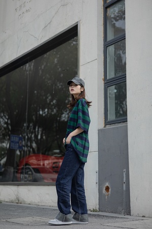 一个穿着牛仔裤、格子衬衫和帽子的女孩站在一栋楼前 另一个人走过