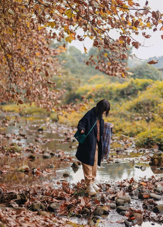 一位妇女站在秋天的水流中 背景中有人行走。