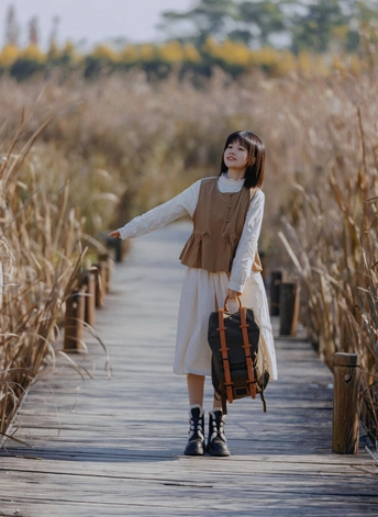 一位年轻女子背着背包站在木桥上 背景是田野。