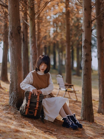 一个年轻女子背着书包坐在一片树木和树叶的森林里的一把椅子上